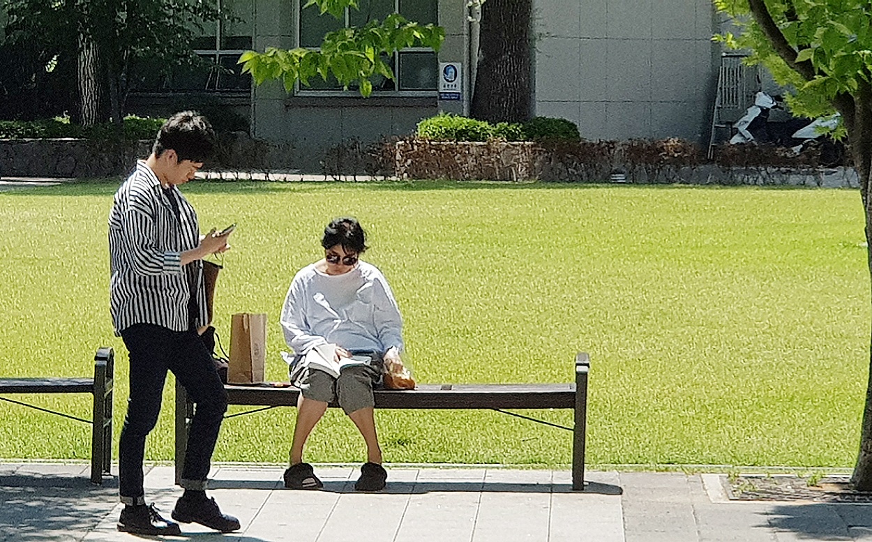 책 읽는 여성 앞으로 걸어서 지나가는 한 행인이 휴대전화를 들여다 보고 있다.(사진=김일현 기자 / 전 스포츠조선 조선일보 사진부 근무)